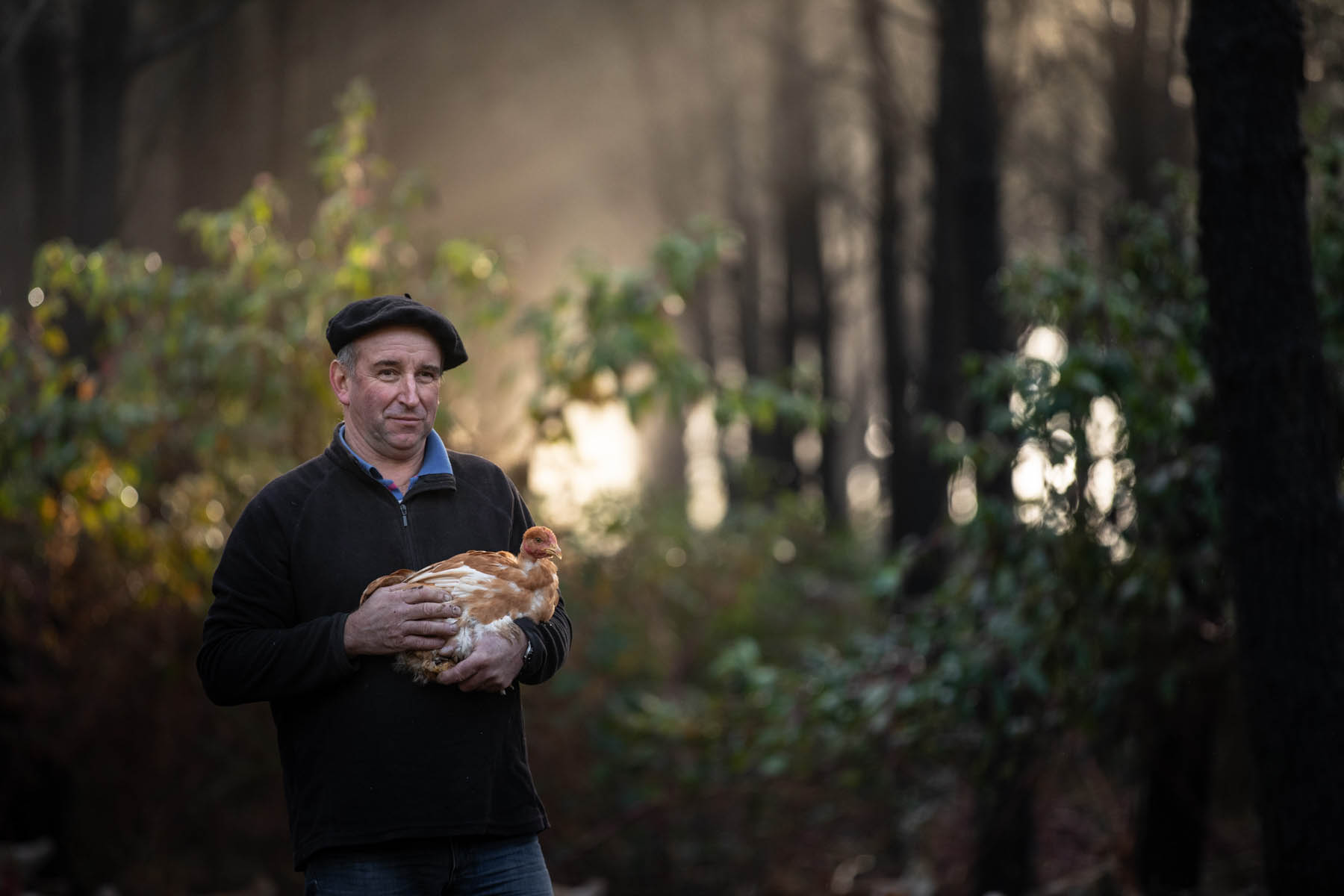 photo d'un fermier landais avec une poule dans les bras au milieu des pins par Carole photographe